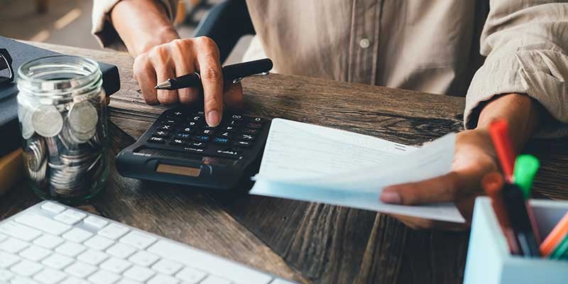 A person uses a calculator while reviewing paper bills at a wooden desk